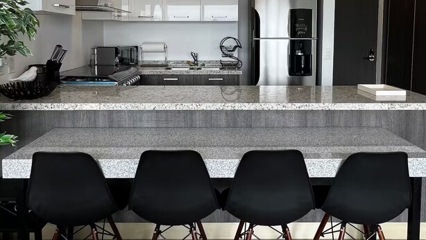 Una cocina moderna con una isla central, electrodomésticos de acero inoxidable y taburetes negros.