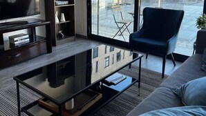 Una sala de estar moderna con un ventanal grande, un sofá, un sillón, un televisor y una estantería.
