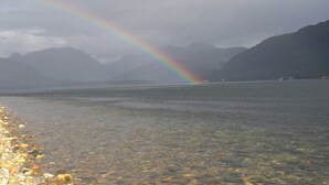 A lake with a rainbow, mountains in the background, and a pebble-strewn shore.