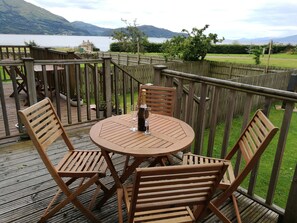 A wooden deck with a round table and chairs, overlooking a lake and mountains. - Cosy cottage in a stunning location - on the shore of Loch Linnhe near Glencoe (Onich)