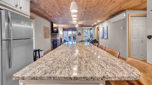 A kitchen with a granite island, stainless steel appliances, wooden ceiling, and a stone fireplace. - Cozy Condo on the Mountain (Sugar Mountain)