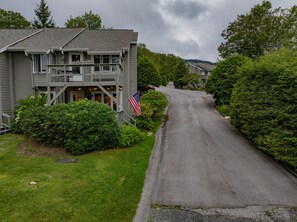 A two-story building with a balcony, a flag, and a driveway leading to another building.