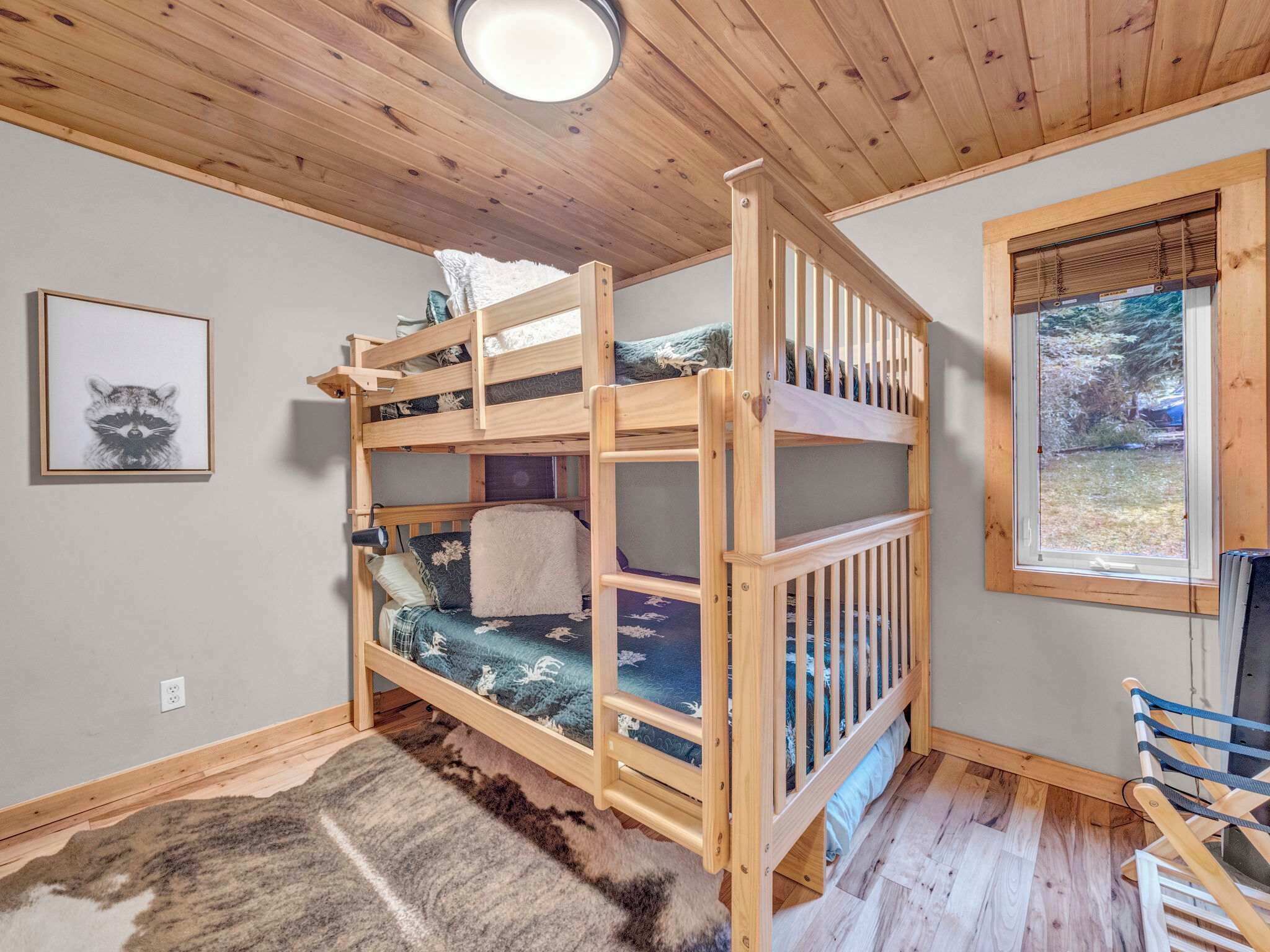A bunk bed with a view of a forest through a window.