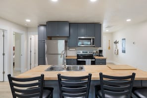 Una cocina moderna con armarios grises, electrodomésticos de acero inoxidable, una isla de madera con sillas y un ventanal grande.