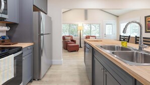 A modern kitchen with grey cabinets, stainless steel appliances, and a wooden countertop. There is a dining area with a chair and a lamp in the background. - Lighthouse Lodge 3 | Lakefront | Sunrise Views + Private Dock | Peaceful Cove (Kimberling City)