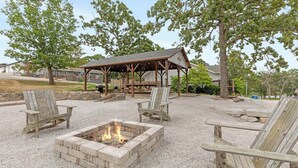Un espace extérieur aménagé avec des sièges couverts, des fauteuils Adirondack, un foyer et une structure en forme de pergola.