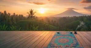 Une terrasse en bois, agrémentée d’un tapis de yoga et de pierres de méditation, offrant une vue sur un paysage luxuriant avec une montagne à l’horizon.