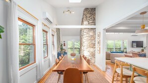 Un comedor amplio con una larga mesa de madera y sillas, ventanas grandes y una pared de acento de piedra.