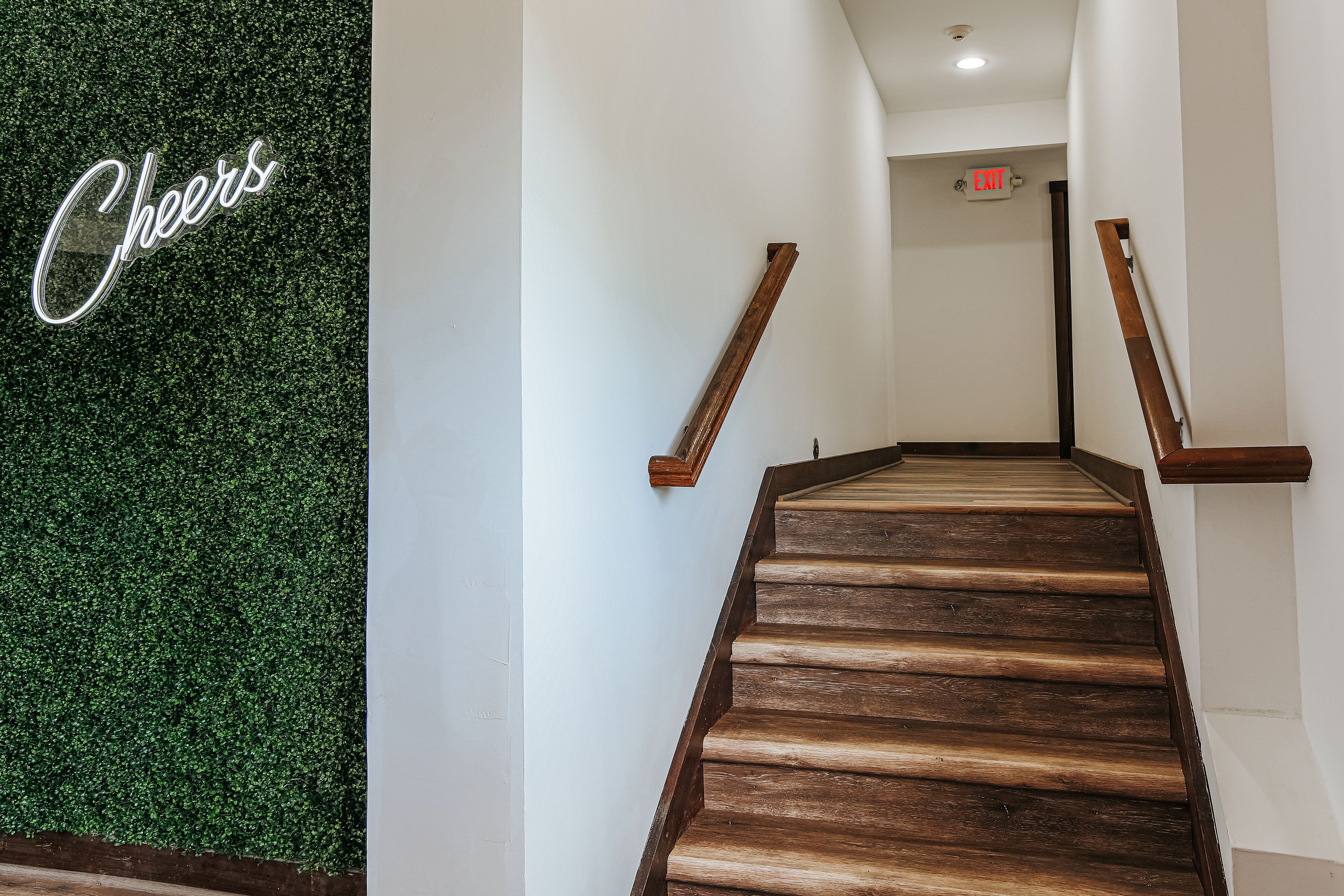 Una escalera de madera con una pared verde y un letrero de neón que dice 'Cheers'.