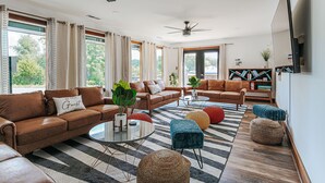 A spacious living room with leather sofas, a striped rug, and a large window with curtains. - ADA King Studio + Roll-in Shower | Pet-Friendly (Afton)