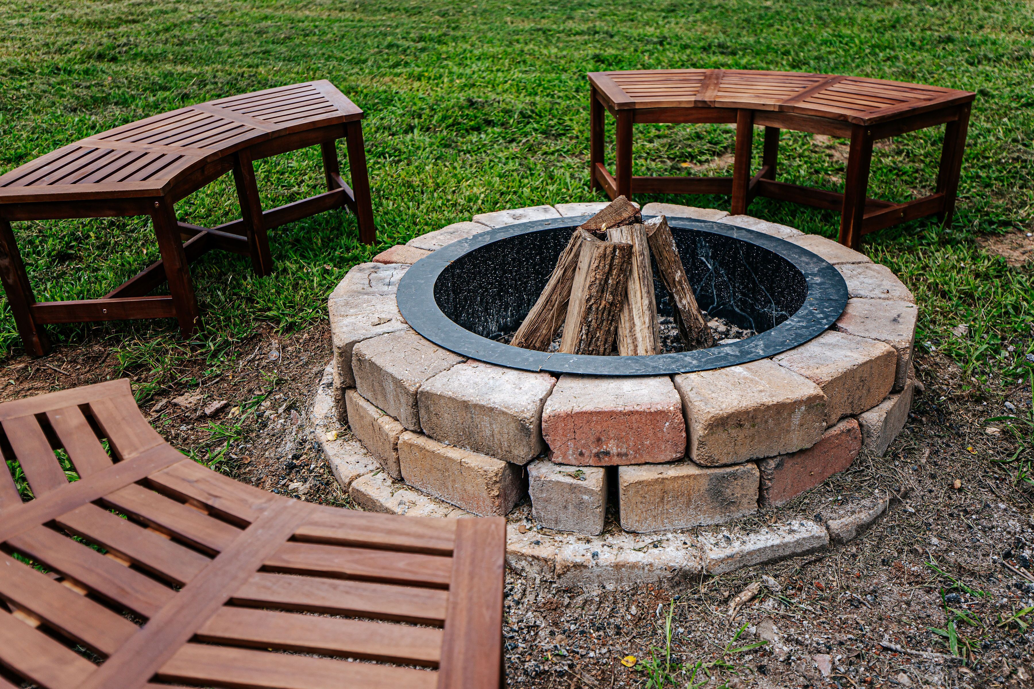 A circular fire pit with a brick surround, surrounded by wooden benches.