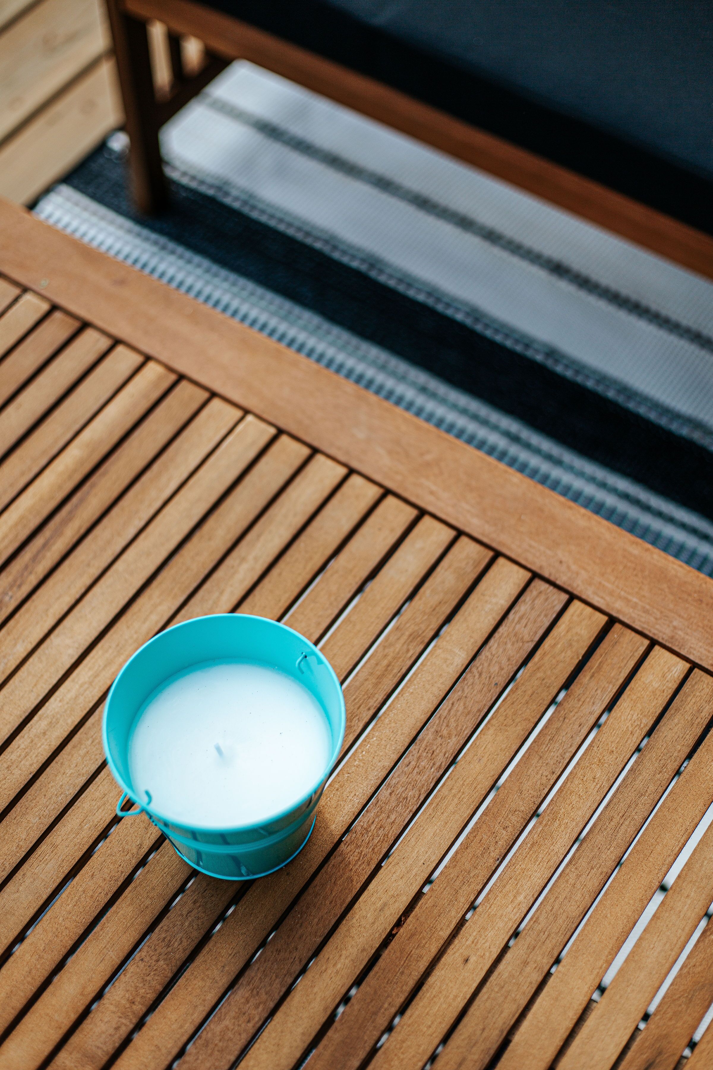 Une table en bois sur laquelle se trouve une tasse bleue contenant un liquide blanc, probablement du lait ou du café, posée sur une terrasse en bois.