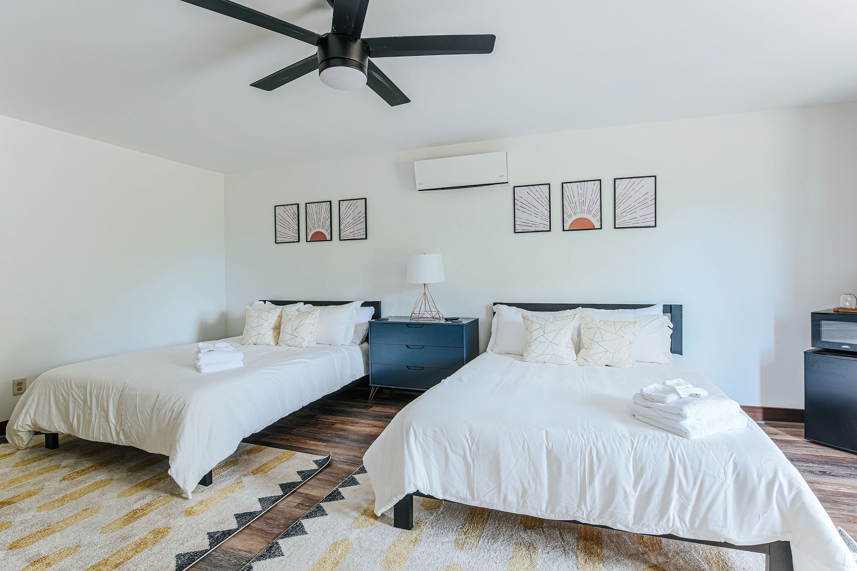 Ein Hotelzimmer mit zwei Betten, einem Deckenventilator, einer Klimaanlage und einem Teppich.