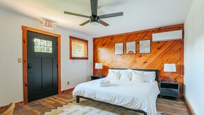 A bedroom with a bed, a ceiling fan, a wooden wall panel, a nightstand, a lamp, and an exit sign. - King Studio w/ Desk & Large Bath | Pet-Friendly (Afton)