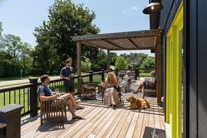 Eine Holzterrasse mit Sitzgelegenheit im Freien, einer Pergola und einem Hund.