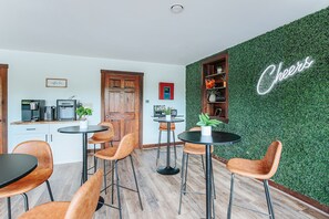Eine moderne Küche mit Kaffeebereich, Barhocker und einem leuchtenden 'Cheers'-Schild an einer grünen Wand.