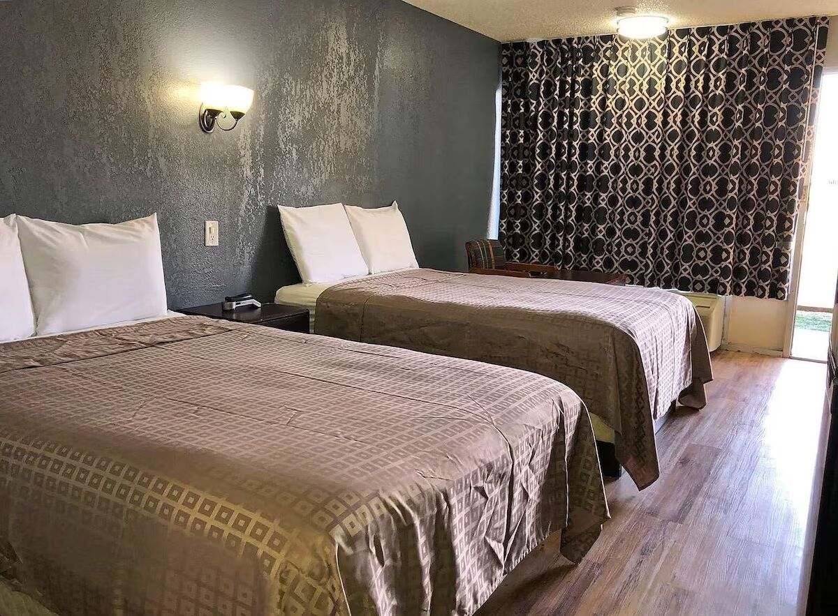 Une chambre avec deux lits, un rideau à motifs et un luminaire fixé au mur.