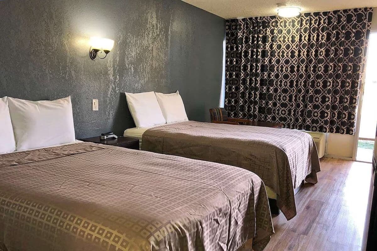 Ein Zimmer mit zwei Betten, einem gemusterten Vorhang und einer Wandleuchte.