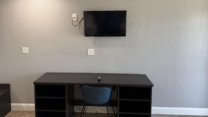 A room with a dark wooden desk, a blue chair, and a mounted flat-screen TV on a textured gray wall. - Best Value Inn Garland (Garland)