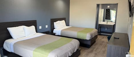 A hotel room with two beds, a small desk, and a mirror.