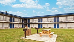 A motel with a courtyard featuring a picnic table and a trash bin. - Best Value Inn Garland (Garland)
