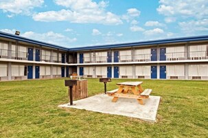 Um motel com um pátio que inclui uma mesa para piquenique e uma lixeira.