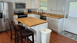 A modern kitchen with white cabinets, a wooden countertop, stainless steel appliances, and a black chair.