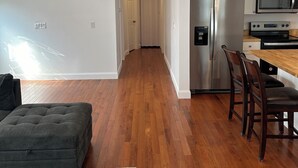 A modern kitchen with stainless steel appliances, a wooden dining table, and a dark grey sofa in a spacious living area with hardwood flooring.