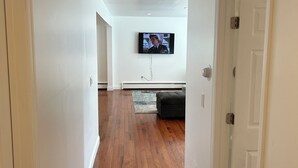 A hallway with hardwood floors, white walls, and a flat-screen TV mounted on the wall.