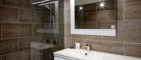 A modern bathroom with a glass-enclosed shower, a large mirror, and a white vanity.