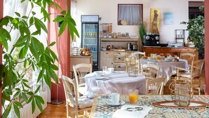 A dining area with a table set for breakfast, a refrigerator, and a kitchen area in the background. - Hotel Le Castellan (Istres)