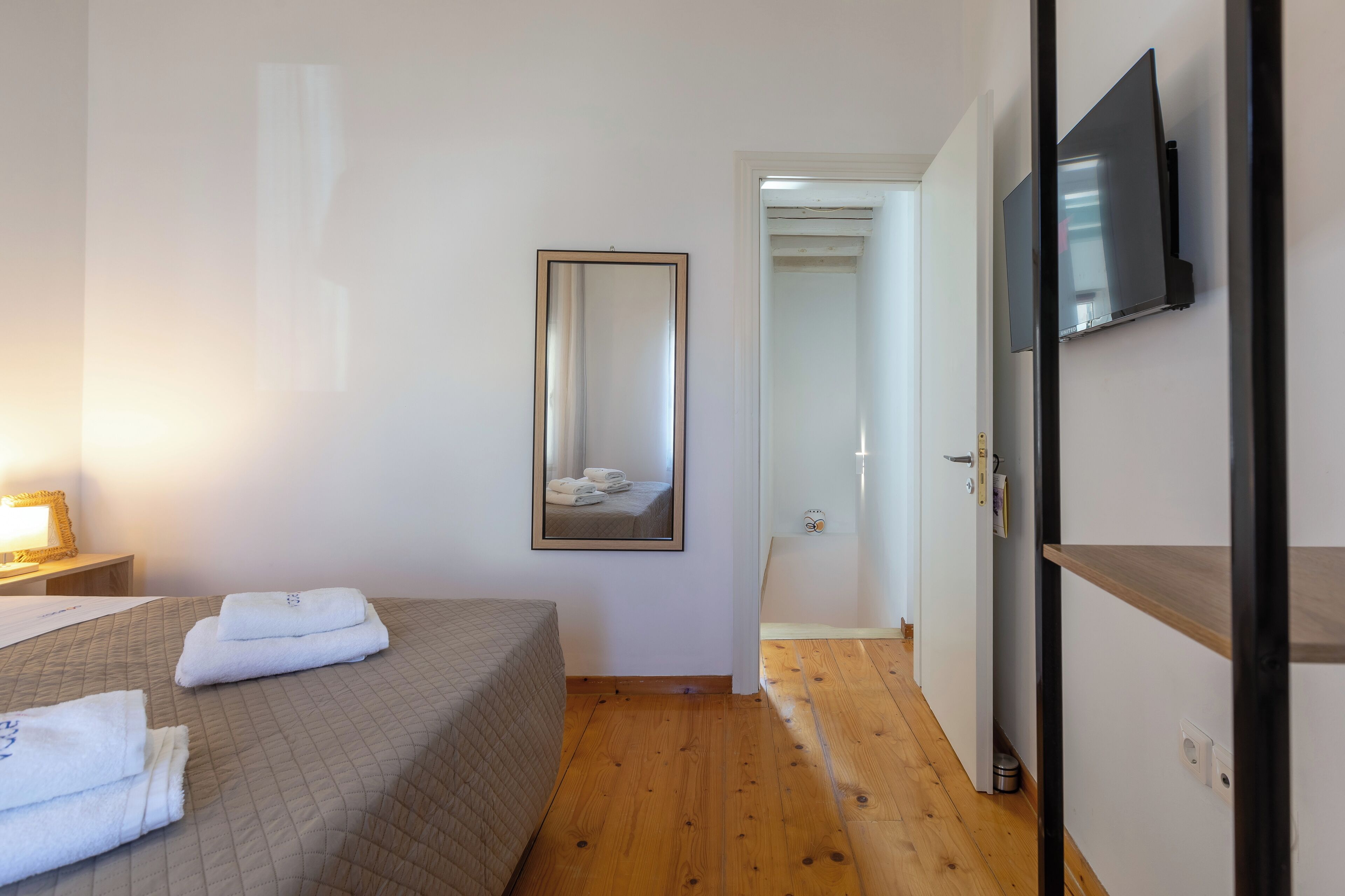 Une chambre d’hôtel avec un lit, un miroir, un téléviseur fixé au mur et un plancher en bois.
