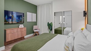 Une chambre d’hôtel moderne avec un mur vert, un grand lit, une commode en bois, une télévision et un miroir.