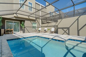 A swimming pool with lounge chairs and a patio area, surrounded by a glass enclosure and beige walls.