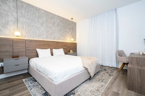 Un dormitorio moderno con una cama grande, mesitas de noche, un escritorio y un ventanal con cortinas.