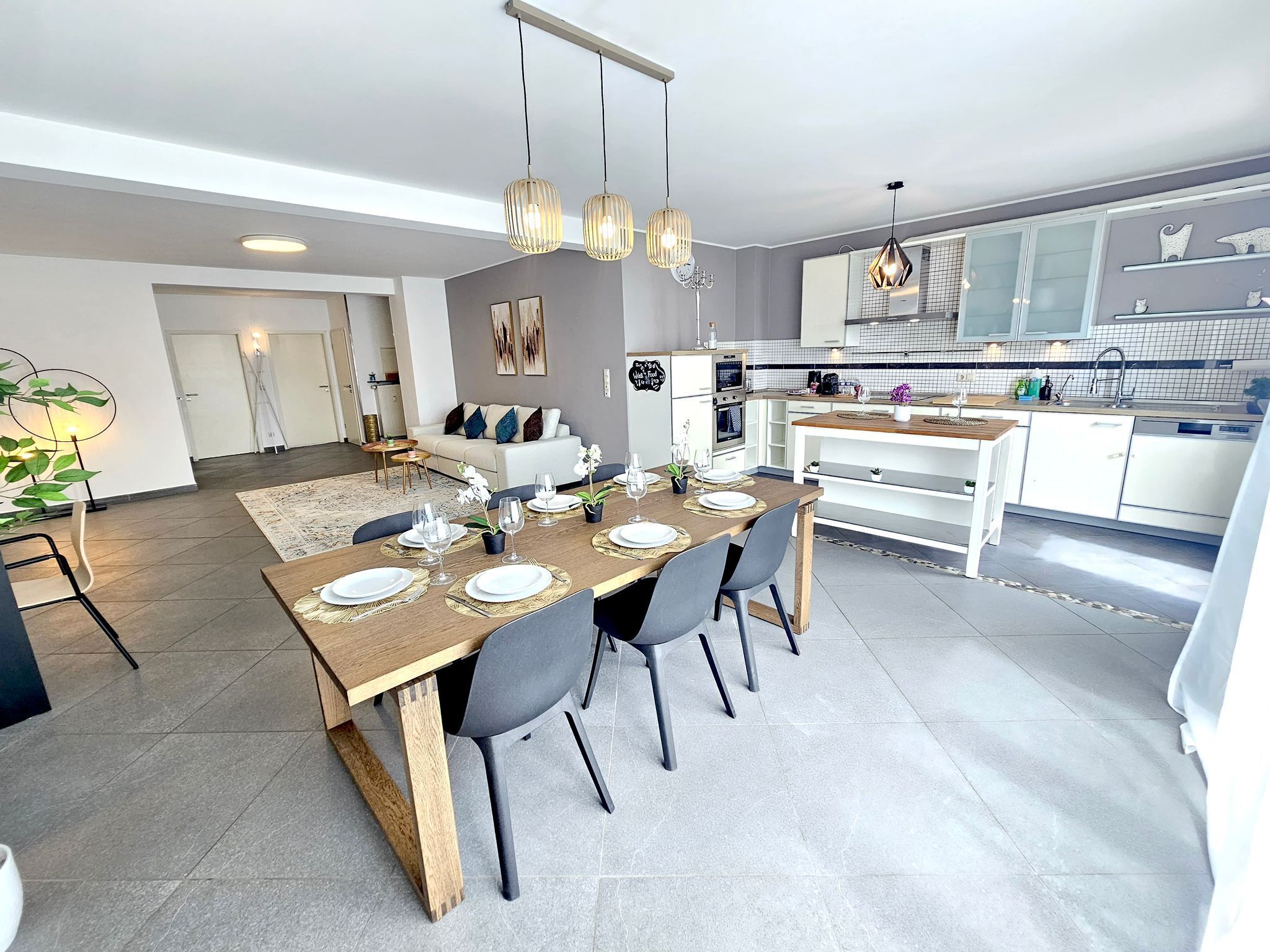 Une cuisine moderne avec des armoires blanches, un four encastré et un coin repas doté d’une table en bois, mise pour quatre personnes.