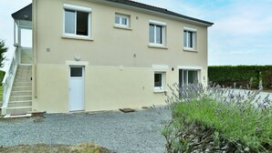 Una casa de dos pisos con fachada color beige, una puerta principal, un porche pequeño y un camino de entrada de grava.