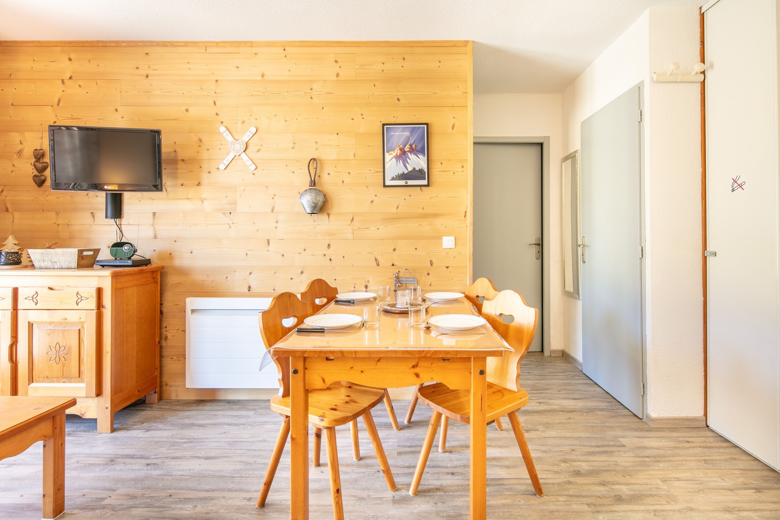 A wooden-paneled room with a dining table set for four, a television, and a small cabinet.
