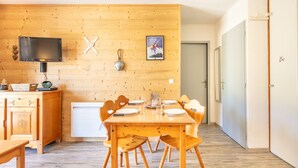 Ein Zimmer mit Holzwänden, einem für vier Personen gedeckten Esstisch, einem Fernseher und einer kleinen Kommode.