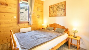 Ein Schlafzimmer aus Holz mit einem Bett, einem Nachttisch, einer Lampe, einem Fenster mit Vorhängen und einer Wandkarte.