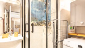 Ein Badezimmer mit Duschkabine aus Glas, Waschbecken, Waschmaschine und Ablage mit Pflegeprodukten.