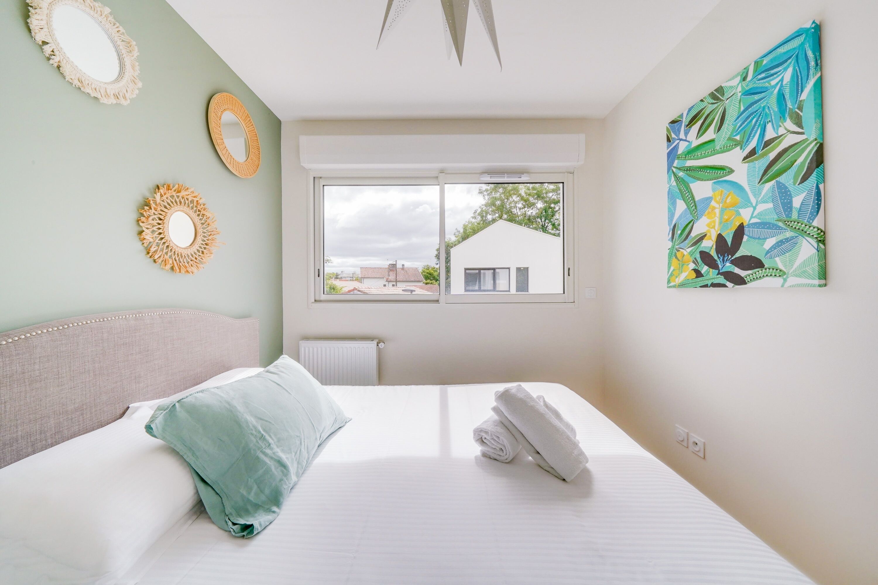 A bedroom with a bed, a window, and a wall with a tropical leaf pattern.