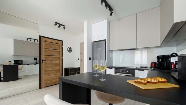 Une cuisine moderne avec un coin repas, comprenant une porte en bois, un plan de travail noir et une chaise.