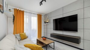 Un salon moderne avec un canapé, une table basse, un téléviseur fixé au mur et une fenêtre avec des rideaux.