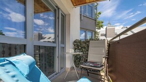 Ein Balkon mit Liegestuhl, einem kleinen Tisch mit Tasse und Untertasse und Blick auf benachbarte Gebäude.