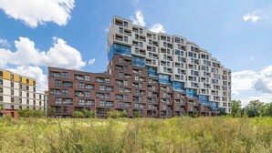 Un immeuble résidentiel à plusieurs étages, doté d’une architecture moderne, avec une façade combinant des éléments en brique et en verre, et un toit plat.