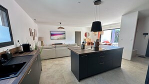 A modern kitchen with a central island, a dining area with a sofa, and a large window providing natural light. - Bastida Provença with private pool (Le Thor)