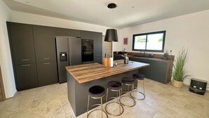 A modern kitchen with a central island, dark cabinetry, and a large window. - Bastida Provença with private pool (Le Thor)