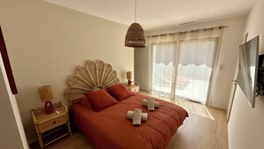 A bedroom with a large bed, a wicker headboard, a bedside table with a lamp, and a large window with curtains. - Bastida Provença with private pool (Le Thor)