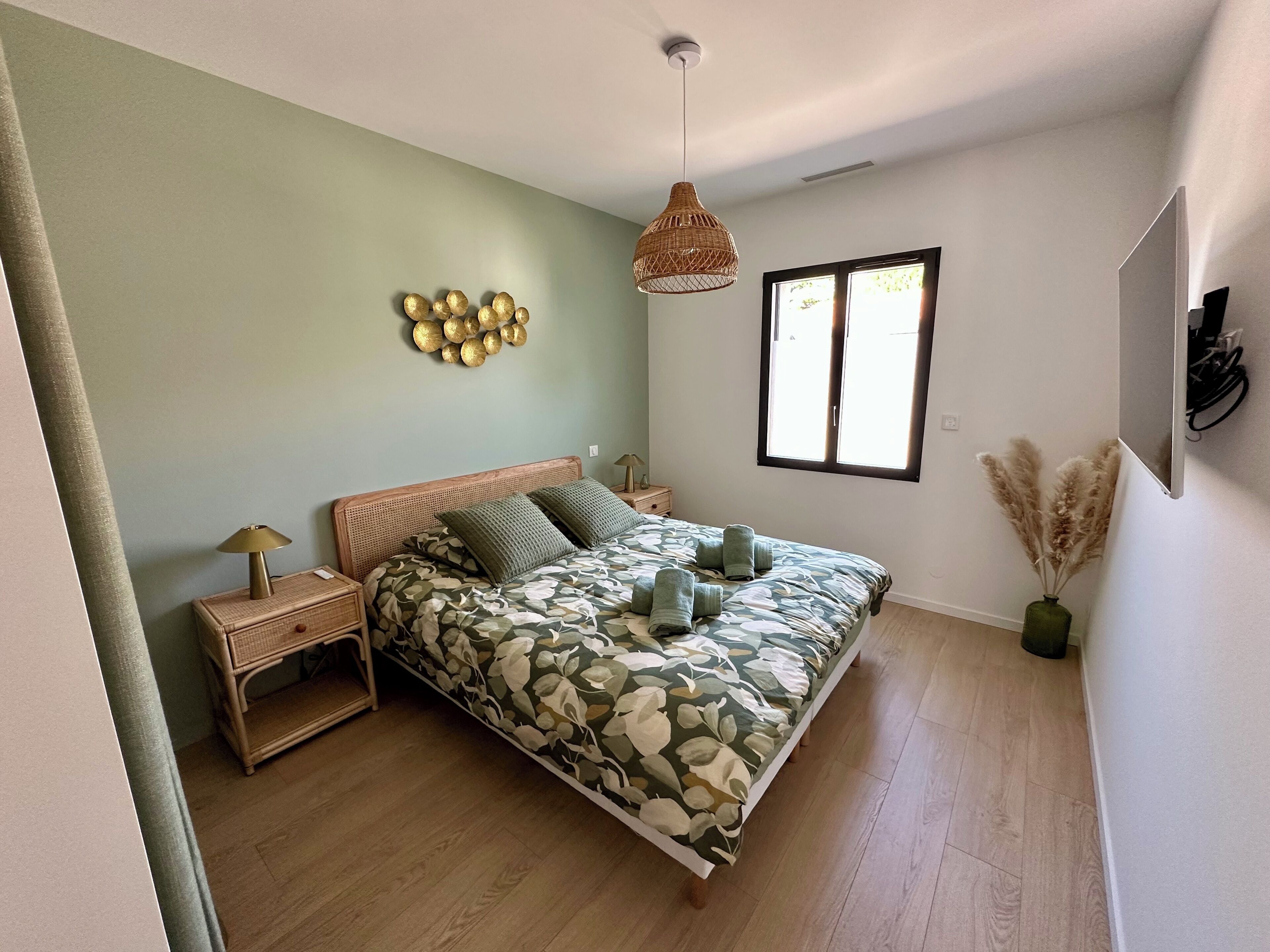 A bedroom with a bed, nightstands, a hanging light, a window, and a wall decoration.